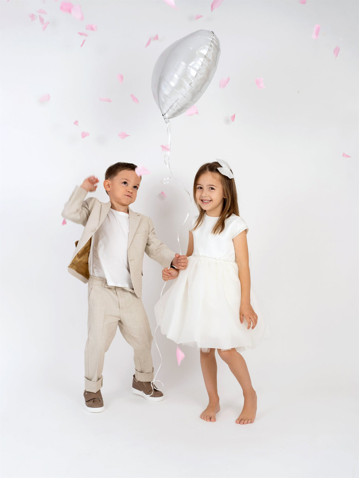 Boy in linen suit and girl in ivory tulle dress celebrating with a balloon